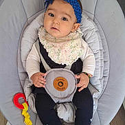 Ralia participe au concours pour gagner de l'argent avec cette photo : accessory, baby, baby_rocker, bib, child, clothing, comfort, curious, cute, floor, footwear, headband, indoor, infant, person, portrait, sitting, soft_furniture, toy, young_child