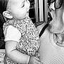 baby, child, adult, glasses, tattoo, floral_dress, indoor, interaction, black_and_white, portrait, person, smile, happy, holding, clothing, face, expression, arm, hand, closeup