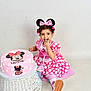 child, toddler, birthday_cake, pink_dress, minnie_mouse, polka_dots, headband, cake, white_background, wicker_stool, celebration, happy, smiling, sitting, party, shoes, cute, indoor, young_child, food