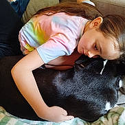 Rocky participe au concours pour gagner de l'argent avec cette photo : child, dog, hugging, couch, blanket, indoor, tie_dye_shirt, black_dog, white_markings, resting, affection, love, comfort, casual_clothing, long_hair, relaxation, pet, friendship, cozy, home