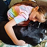 child, dog, hugging, couch, blanket, indoor, tie_dye_shirt, black_dog, white_markings, resting, affection, love, comfort, casual_clothing, long_hair, relaxation, pet, friendship, cozy, home