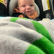 Finnley is registered to the contest to win money with this photo: baby, car_seat, blanket, smiling, infant, face, child, seatbelt, clothing, head, cozy, indoor, portrait, cute, safety, young_child, expression, human, closeup, car