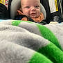 baby, car_seat, blanket, smiling, infant, face, child, seatbelt, clothing, head, cozy, indoor, portrait, cute, safety, young_child, expression, human, closeup, car