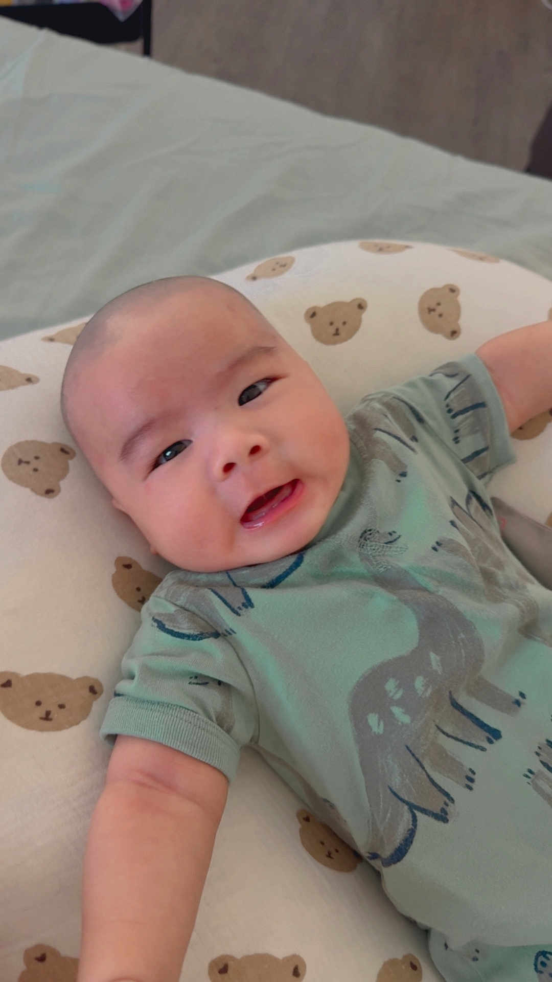 Kilian joined the competition — help win amazing prizes! baby, infant, child, cute, smiling, green_shirt, dinosaur_print, bear_pattern, cushion, lying_down, arm, face, happy, indoors, soft_toy_pattern, childhood, adorable, young, person, portrait