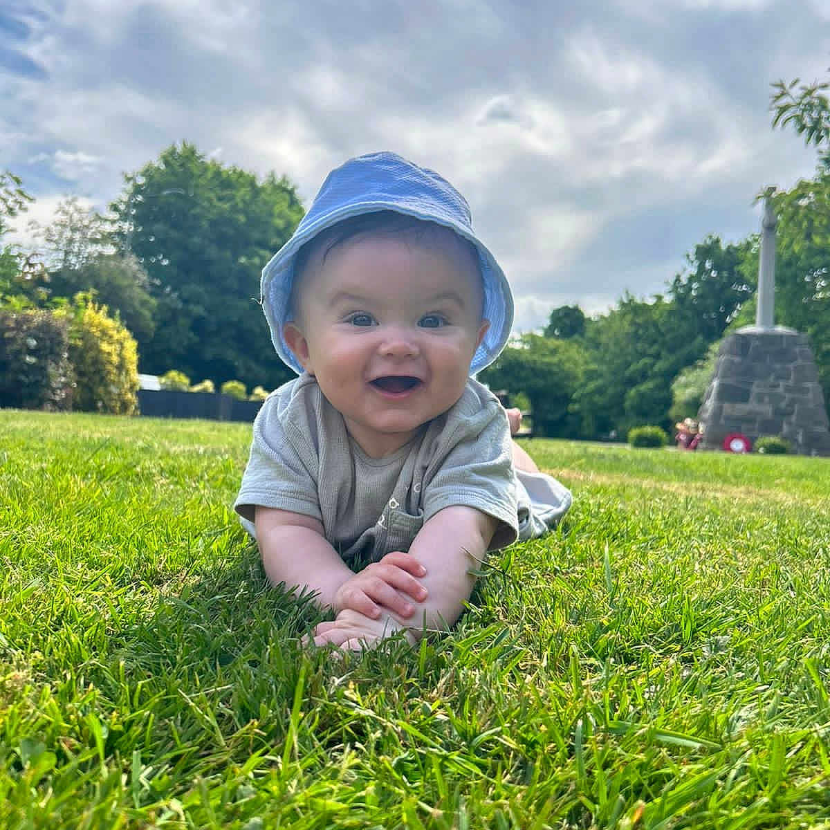 Shea is registered to the contest to win money with this photo: baby, casual_clothing, child, clouds, crawling, daylight, grass, greenery, happy, hat, monument, nature, outdoor, person, portrait, sky, smiling, summer, sunhat, trees