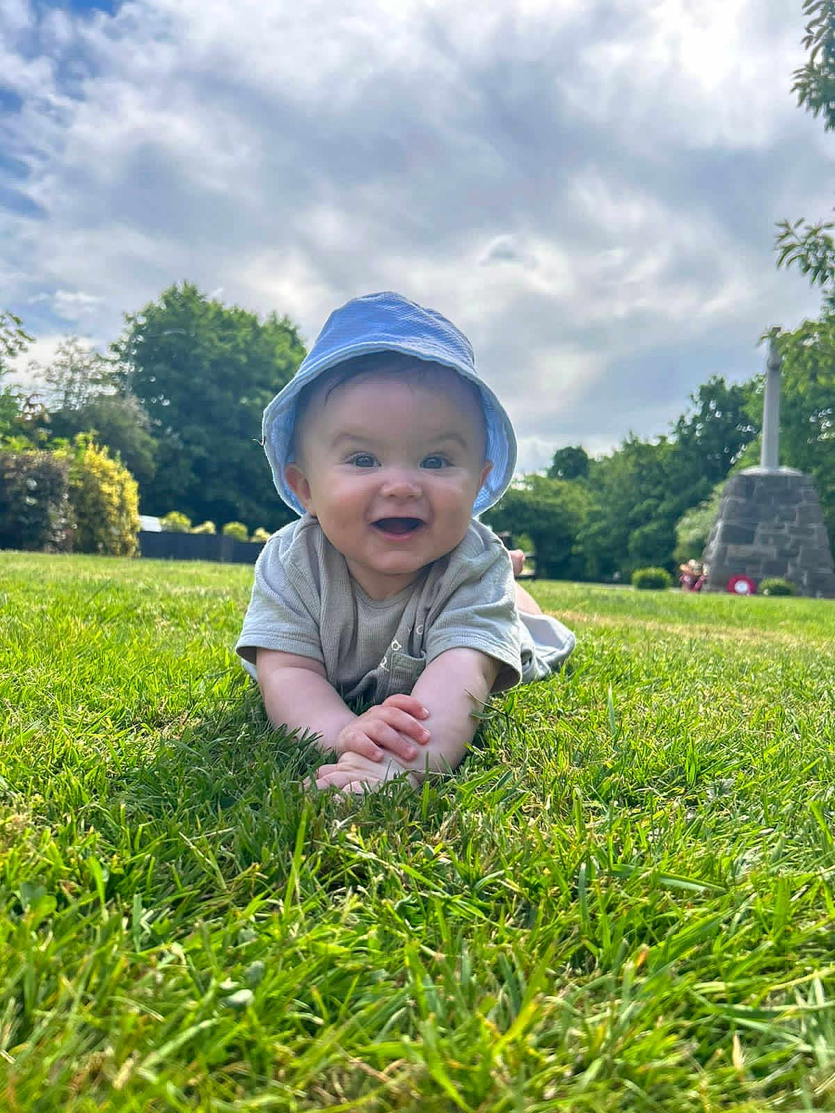 Shea is registered to the contest to win money with this photo: baby, child, grass, outdoor, smiling, hat, sunhat, greenery, sky, clouds, trees, nature, happy, portrait, person, summer, crawling, monument, daylight, casual_clothing