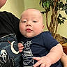 Ryder joined the competition — help win amazing prizes! baby, child, person, indoor, plant, green_leaves, navy_shirt, graphic_tee, hand, face, curious, skin, tattoo, holding, light_yellow_wall, portrait, casual_clothing, plush, relaxed, closeup