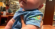 Ryder joined the competition — help win amazing prizes! baby, child, infant, person, blue_clothing, library, bookshelf, table, arm, hand, indoor, curious_expression, chubby_cheeks, lighting, adult, technology, phone, furniture, holding, portrait