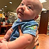 adult, arm, baby, blue_clothing, bookshelf, child, chubby_cheeks, curious_expression, furniture, hand, holding, indoor, infant, library, lighting, person, phone, portrait, table, technology