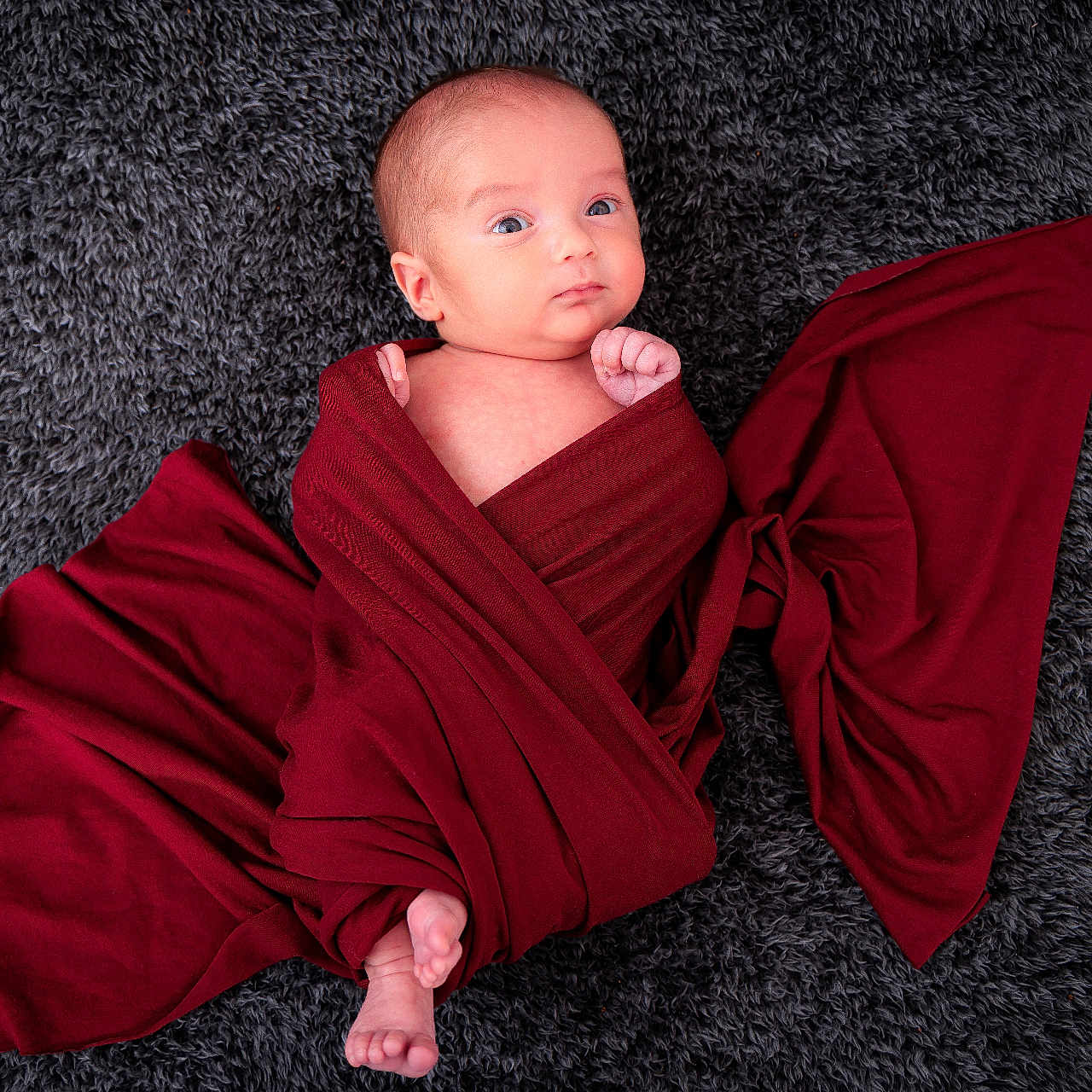 Andréa participe au concours pour gagner de l'argent avec cette photo : baby, carpet, child, cozy, cute, expression, face, floor, foot, hand, indoors, infant, lying_down, newborn, person, portrait, red_cloth, skin, soft_texture, wrapped