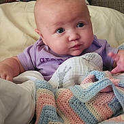 Phenoix joined the competition — help win amazing prizes! baby, infant, purple_clothing, blanket, crochet_blanket, pastel_colors, bed, headboard, soft_texture, curious_expression, chubby_cheeks, person, indoor, cozy, child, newborn, cute, face, cuddly, resting