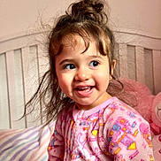 Dafne is registered to the contest to win money with this photo: bed, child, colorful, cozy, cute, face, hair_bun, happy, indoors, messy_hair, onesie, pajamas, pink, plush_toy, portrait, smiling, soft_lighting, toddler, unicorn, young_child