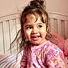 toddler, child, smiling, bed, pajamas, onesie, unicorn, pink, hair_bun, happy, indoors, plush_toy, cozy, cute, portrait, young_child, face, messy_hair, colorful, soft_lighting