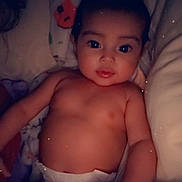 London-Dior is registered to the contest to win money with this photo: baby, infant, child, diaper, lying_down, portrait, face, wide_eyed, dark_hair, brown_skin, blanket, bed, plush_toy, heart, sparkles, indoor, cozy, close_up, adorable, photography