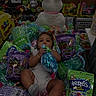 baby, candy, plush_bunny, decorative_grass, shopping_cart, packaging, child, toy_store, snack, colorful, retail, grocery, product_packaging, sitting, infant, cute, store_shelf, retail_display, playful, holding