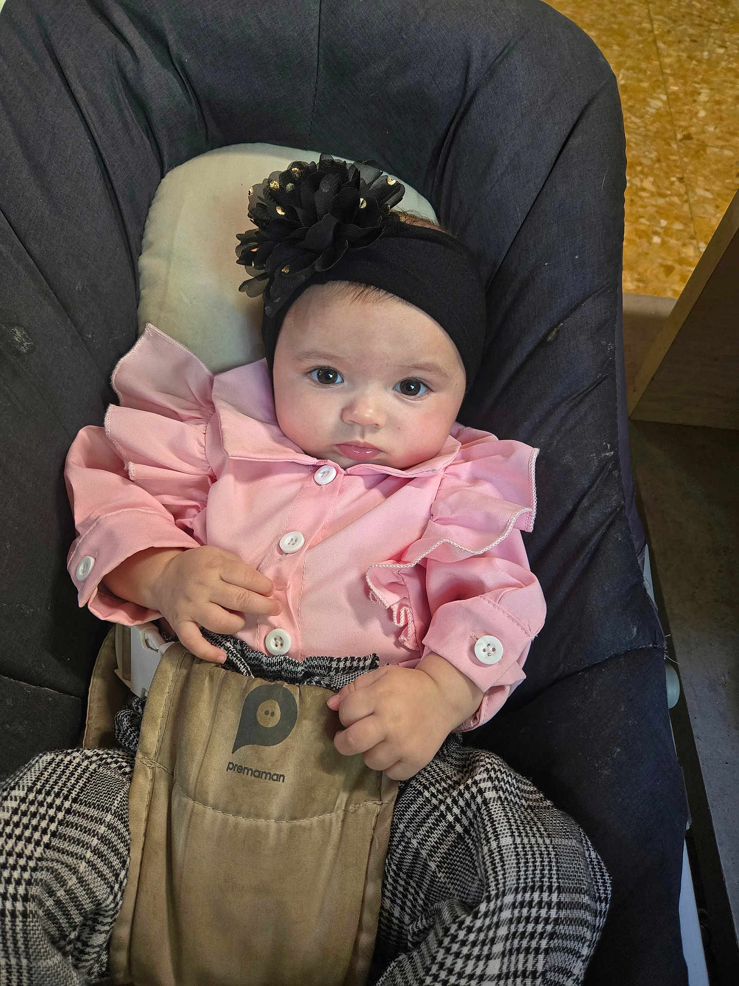 Gabriella participe au concours pour gagner de l'argent avec cette photo : baby, child, infant, pink_clothing, headband, flower, baby_carrier, checkered_pants, sitting, indoors, floor, face, hands, person, cute, young, portrait, looking, clothing, fabric