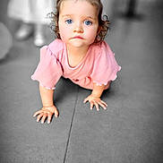 Ambre a rejoint le concours — aidez-le/la à gagner de superbes lots ! toddler, child, crawling, blue_eyes, pink_clothing, curly_hair, indoor, floor_tiles, baby, person, cute, portrait, young_child, hair_bow, focused, hands, kneeling, blurred_background, indoor_lighting, curious