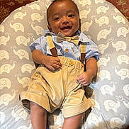 Reagan joined the competition — help win amazing prizes! baby, infant, smiling, face, blue_socks, bow_tie, suspenders, shorts, patterned_mat, elephant_pattern, cushion, carpet, happy, cute, indoors, child, portrait, clothing, legs, hands