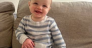 Cade is registered to the contest to win money with this photo: baby, child, smiling, striped_pajamas, couch, beige, indoor, family_photos, wall, framed_photos, happy, portrait, sitting, feet, furniture, infant, cute, home, person, cozy