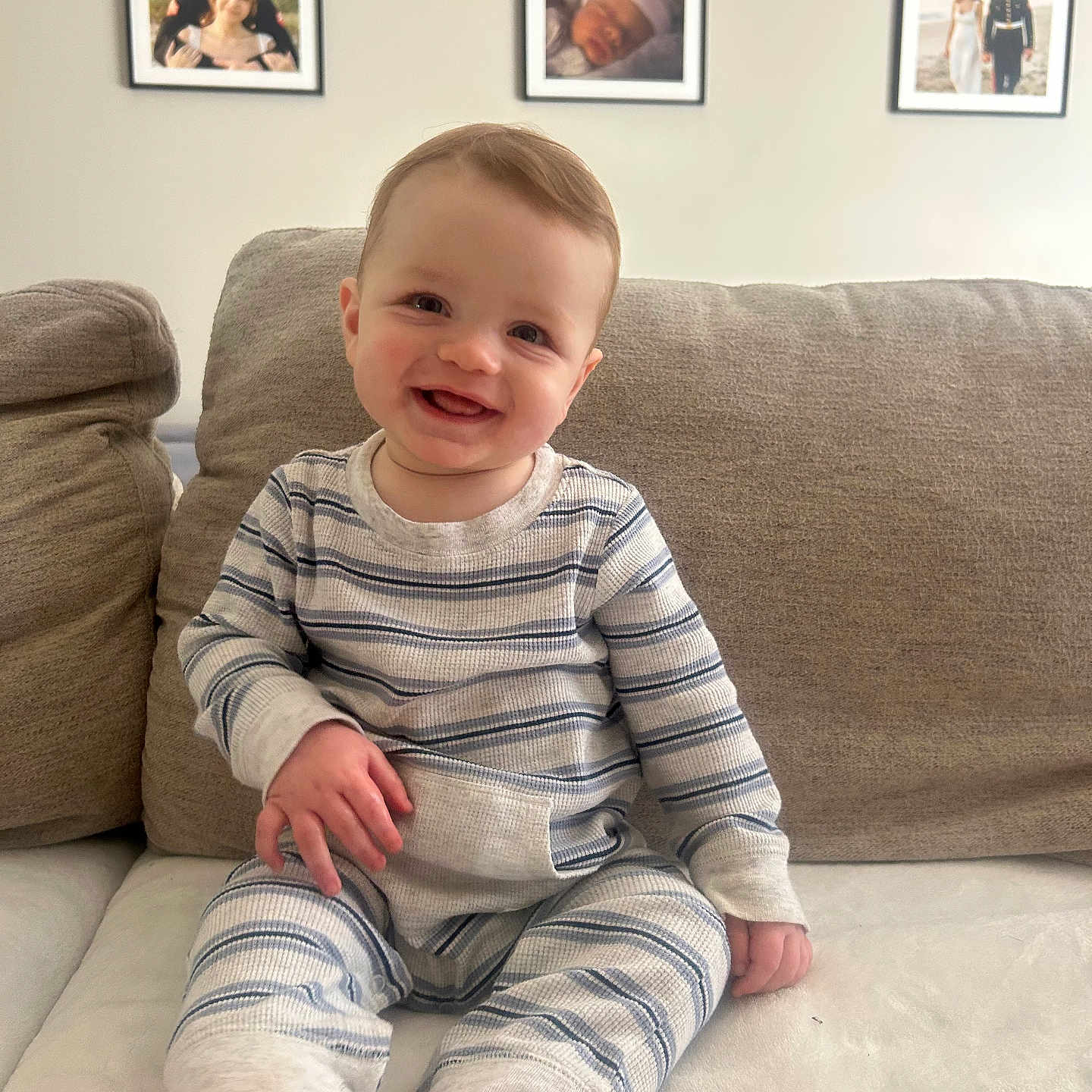 Cade is registered to the contest to win money with this photo: baby, child, smiling, striped_pajamas, couch, beige, indoor, family_photos, wall, framed_photos, happy, portrait, sitting, feet, furniture, infant, cute, home, person, cozy