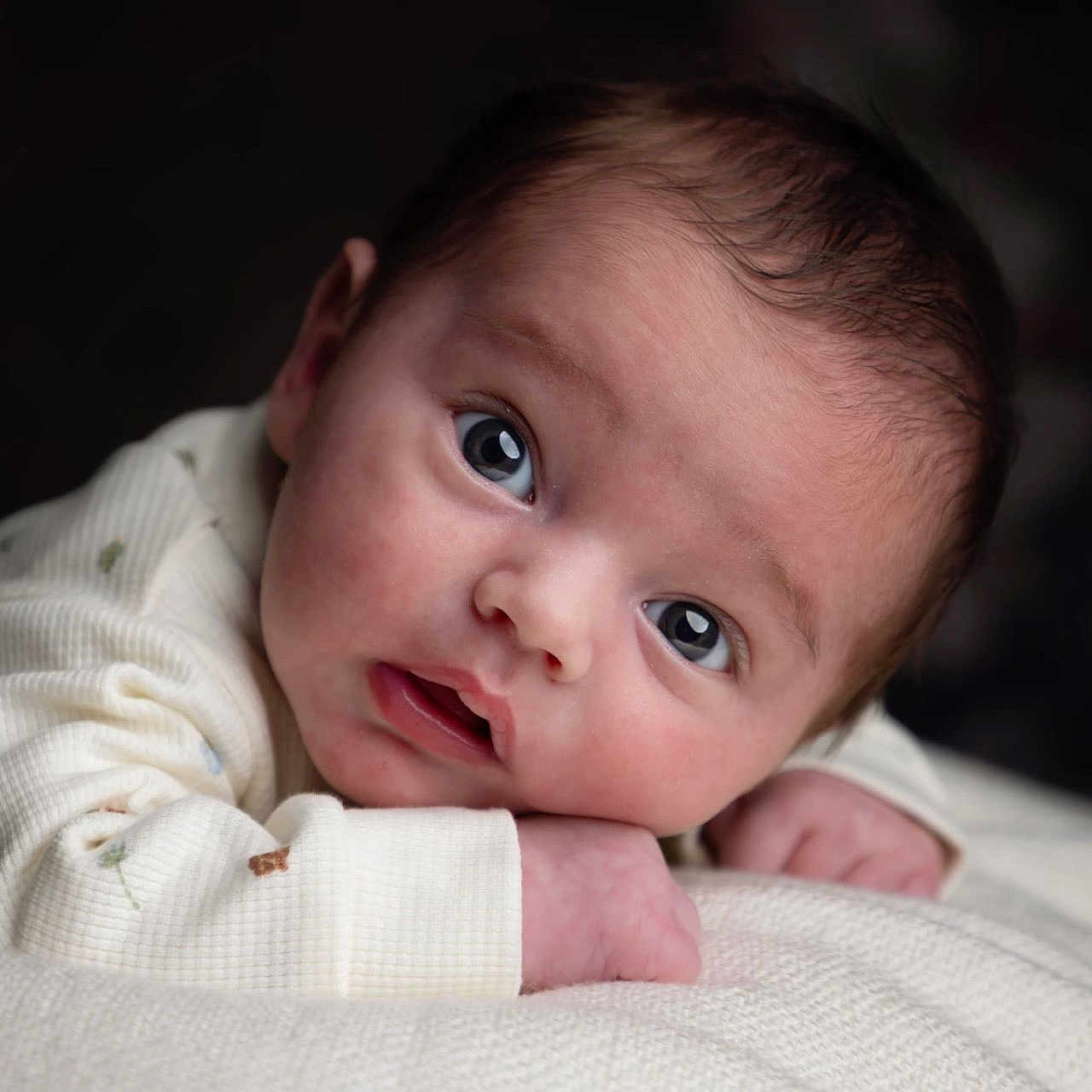 Nael a rejoint le concours — aidez-le/la à gagner de superbes lots ! baby, baby_gaze, closeup, cozy, curious, cute, dark_background, expression, eyes, face, hands, head, infant, lying_down, newborn, portrait, skin, soft_texture, white_clothing, young_child