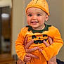 Luna a rejoint le concours — aidez-le/la à gagner de superbes lots ! baby, child, pumpkin_costume, orange_clothing, hat, smile, happy, hands, indoor, person, cute, festive, holiday, portrait, face, costume, holding, cheerful, young_child, celebration