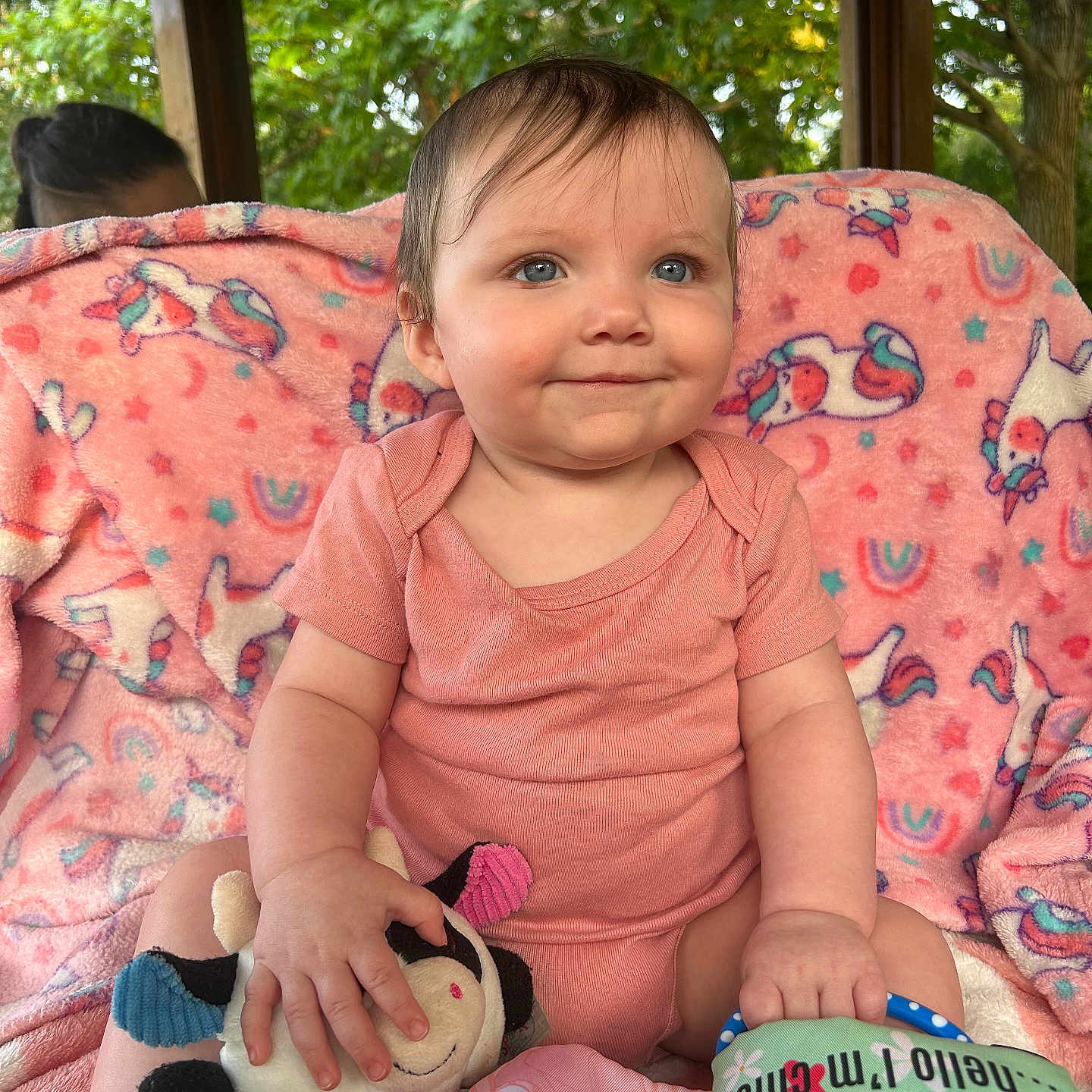 Rowyn is registered to the contest to win money with this photo: baby, blanket, blue_eyes, child, colorful, cute, gazebo, greenery, happy, infant, outdoor, pink_onesie, playful, plush_toy, portrait, seated, smiling, soft_toy, toy, unicorn_blanket