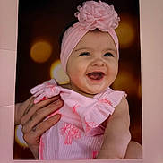 Evy is registered to the contest to win money with this photo: baby, child, pink_headband, flower, dress, smile, laughing, hand, bokeh, portrait, infant, cute, happy, closeup, face, person, apparel, headwear, skin, background