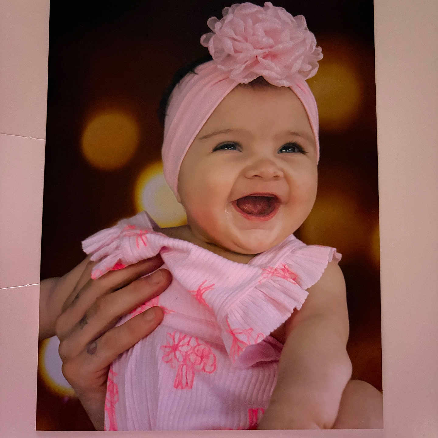 Evy is registered to the contest to win money with this photo: baby, child, pink_headband, flower, dress, smile, laughing, hand, bokeh, portrait, infant, cute, happy, closeup, face, person, apparel, headwear, skin, background