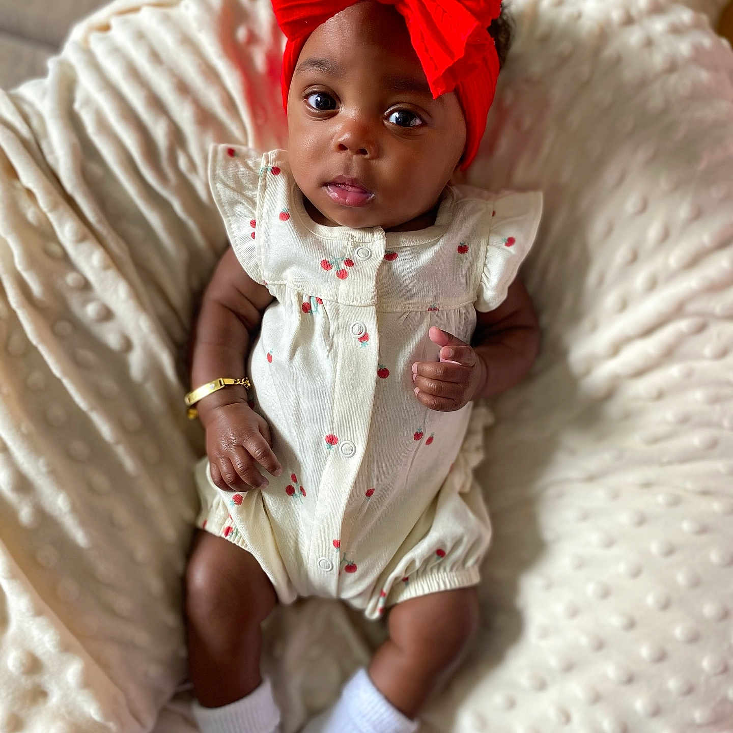 Charli is registered to the contest to win money with this photo: adorable, baby, blanket, bracelet, child, comfortable, cute, flower, headband, indoors, infant, large_eyes, lying_down, portrait, red_bow, romper, skin, small_hands, soft_texture, white_socks