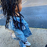 Alani is registered to the contest to win money with this photo: child, denim_jacket, braided_hair, jeans, sneakers, white_shoes, nike, side_view, outdoor, pavement, curious, young_child, fashion, street_style, casual, person, standing, daylight, fence, patches