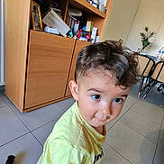 Gauthier participe au concours pour gagner de l'argent avec cette photo : toddler, child, curly_hair, yellow_shirt, indoor, floor_tiles, cabinet, furniture, curious, big_eyes, person, young_child, home, casual_clothing, brown_hair, hair, standing, room, household_items, light