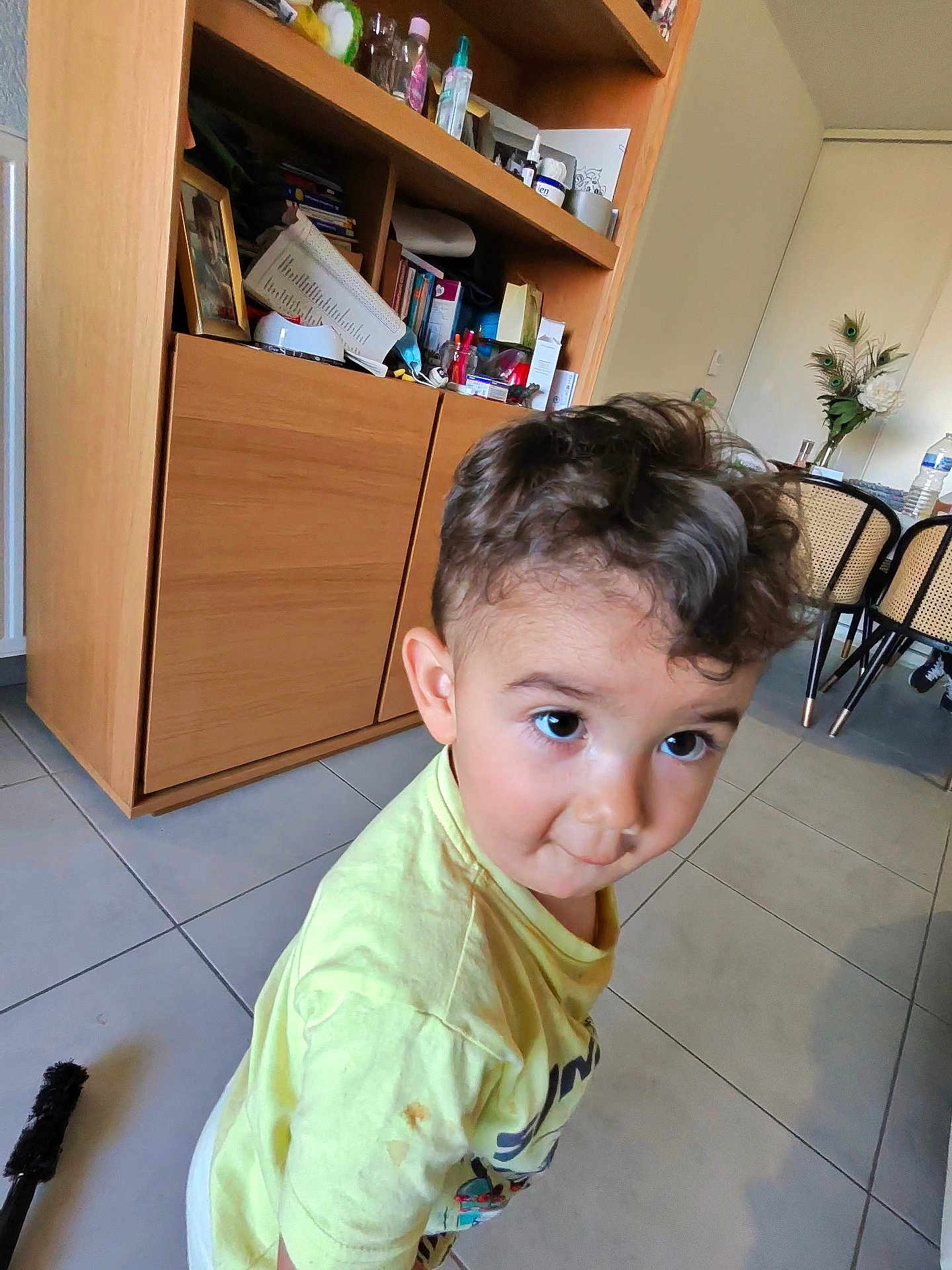 Gauthier participe au concours pour gagner de l'argent avec cette photo : toddler, child, curly_hair, yellow_shirt, indoor, floor_tiles, cabinet, furniture, curious, big_eyes, person, young_child, home, casual_clothing, brown_hair, hair, standing, room, household_items, light