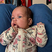 Emder is registered to the contest to win money with this photo: baby, infant, newborn, onesie, floral_pattern, blue_lap, hand_in_mouth, wide_eyes, surprised_expression, portrait, indoor, bedroom, closet, clothes_hangers, mask_on_wall, cute, skin_tone, head, eyes, sitting