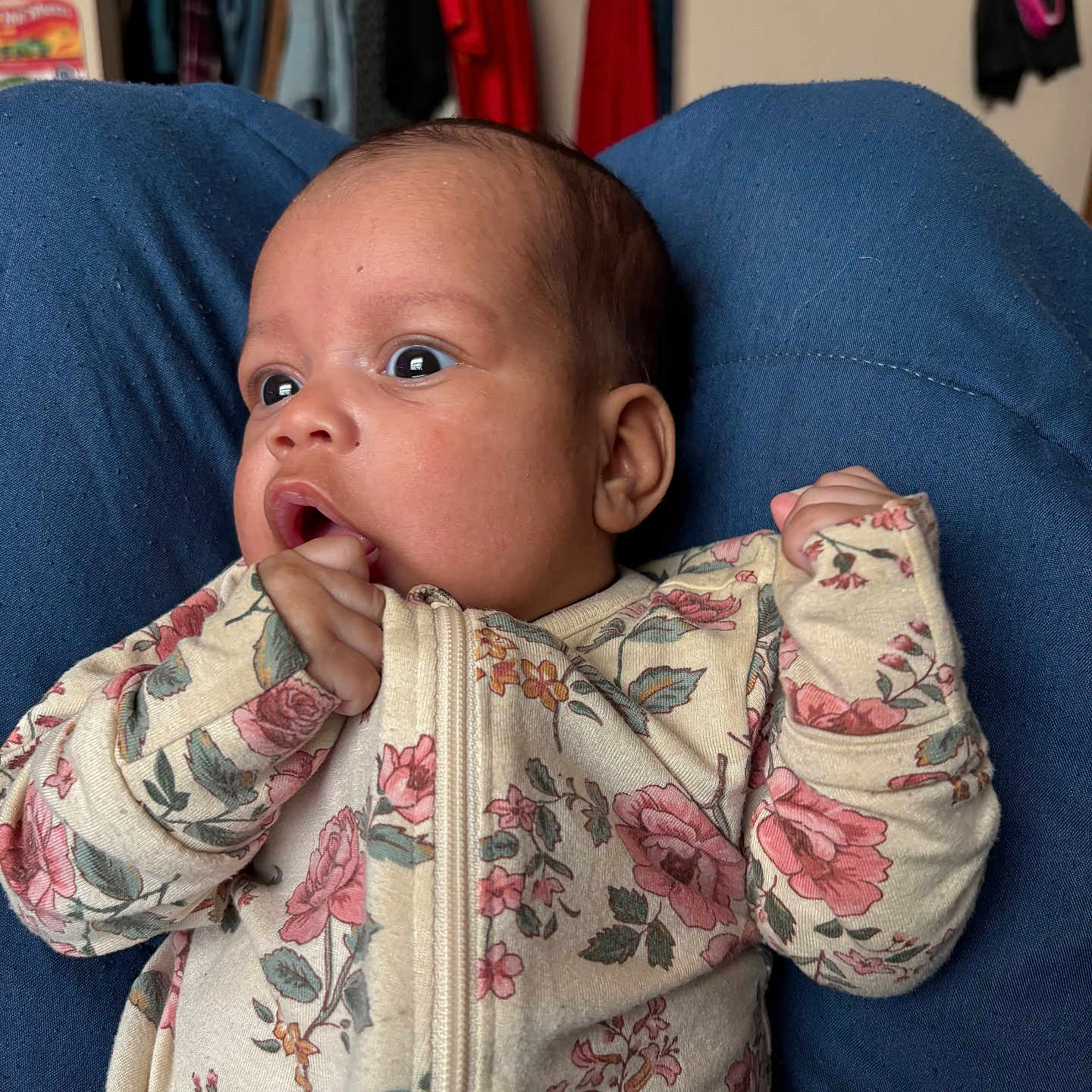 Emder is registered to the contest to win money with this photo: baby, bedroom, blue_lap, closet, clothes_hangers, cute, eyes, floral_pattern, hand_in_mouth, head, indoor, infant, mask_on_wall, newborn, onesie, portrait, sitting, skin_tone, surprised_expression, wide_eyes