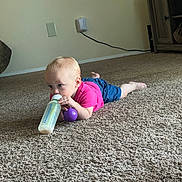 Sophie is registered to the contest to win money with this photo: toddler, baby, carpet, floor, bottle, toy, purple, pink_shirt, blue_shorts, indoor, child, person, crawling, curious, home, cabinet, wall, power_outlet, foot, head