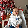 toddler, child, smile, white_shirt, blue_jeans, chair, christmas_tree, ornaments, gifts, holiday, indoor, decorations, festive, red, white, present, table, happy, person, celebration