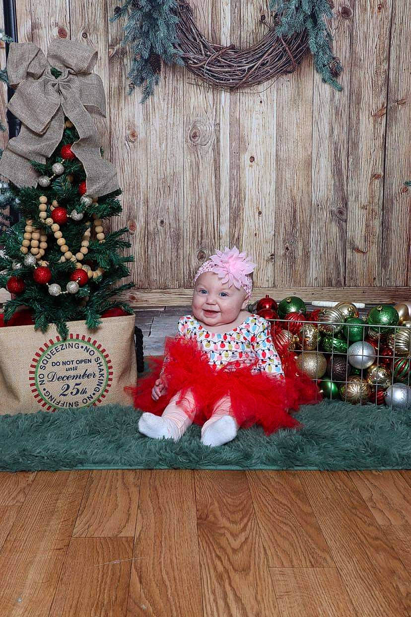 Blakelyn joined the competition — help win amazing prizes! baby_toddler_clothing, christmas, christmas_decoration, christmas_eve, christmas_ornament, christmas_tree, conifer, event, evergreen, headwear, holiday, holiday_ornament, home, joy, ornament, person, plant, sitting, smile, toddler