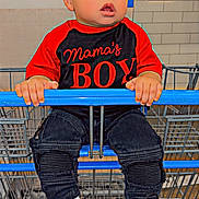 Jayden is registered to the contest to win money with this photo: toddler, child, shopping_cart, curly_hair, red_shirt, black_pants, sneakers, indoor, store, tiles, hands, face, expression, clothing, person, footwear, cute, young_child, casual, curious