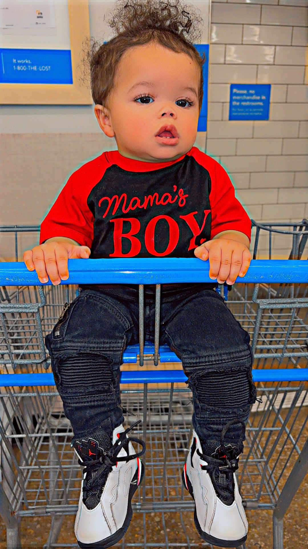 Jayden is registered to the contest to win money with this photo: toddler, child, shopping_cart, curly_hair, red_shirt, black_pants, sneakers, indoor, store, tiles, hands, face, expression, clothing, person, footwear, cute, young_child, casual, curious