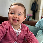 Elena participe au concours pour gagner de l'argent avec cette photo : baby, child, smiling, indoor, pink_sweater, happy, portrait, face, person, clothing, seated, cozy, cute, infant, young_child, background_blur, home, expression, joy, reaching_out