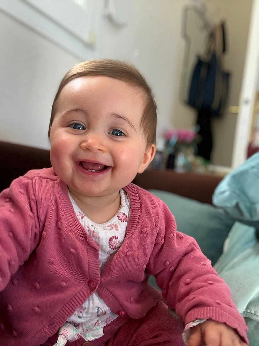 Elena participe au concours pour gagner de l'argent avec cette photo : baby, child, smiling, indoor, pink_sweater, happy, portrait, face, person, clothing, seated, cozy, cute, infant, young_child, background_blur, home, expression, joy, reaching_out