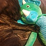 dog, plush_toy, dinosaur, blue, green, black, furry, pet, cuddle, soft_toy, animal, indoor, blurred, paw, texture, fabric, sleeping, resting, close_up, cozy