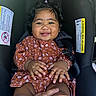 baby, black_hair, car_seat, child, closeup, clothing, cute, dress, hand, happy, indoors, infant, pattern, person, portrait, seat_belt, sitting, skin, smiling, young