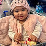 aisle, baby, child, clothing, curly_hair, cute, face, hand, happy, indoor, infant, jingle_bells, knit_hat, person, pink_vest, shopping_cart, sitting, smile, store, toy