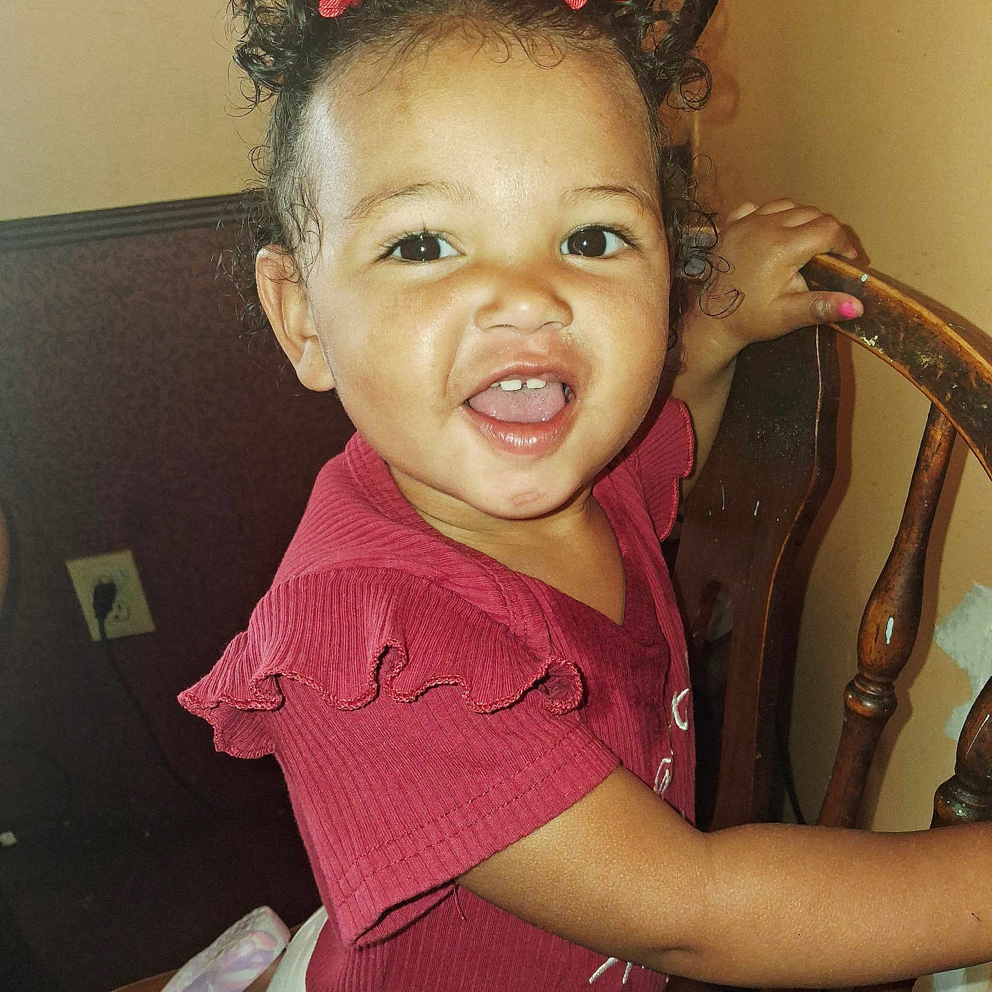 Brailey is registered to the contest to win money with this photo: candid, child, curly_hair, cute, expression, face, furniture, hair_clips, hand, happy, home, indoor, person, portrait, red_clothing, skin, smiling, toddler, wooden_chair, young_child