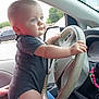 baby, child, car, steering_wheel, hands, blue_eyes, onesie, interior, vehicle, window, side_mirror, seat, person, cute, curious, infant, driving, dashboard, beads, hand