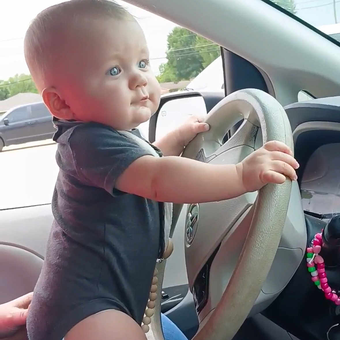 Easton is registered to the contest to win money with this photo: baby, beads, blue_eyes, car, child, curious, cute, dashboard, driving, hand, hands, infant, interior, onesie, person, seat, side_mirror, steering_wheel, vehicle, window