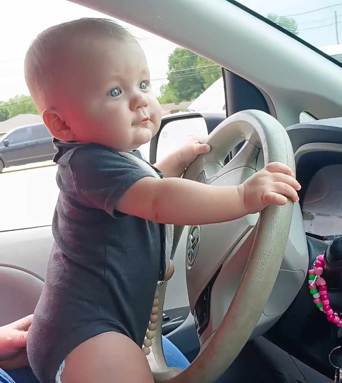 Easton is registered to the contest to win money with this photo: baby, child, car, steering_wheel, hands, blue_eyes, onesie, interior, vehicle, window, side_mirror, seat, person, cute, curious, infant, driving, dashboard, beads, hand