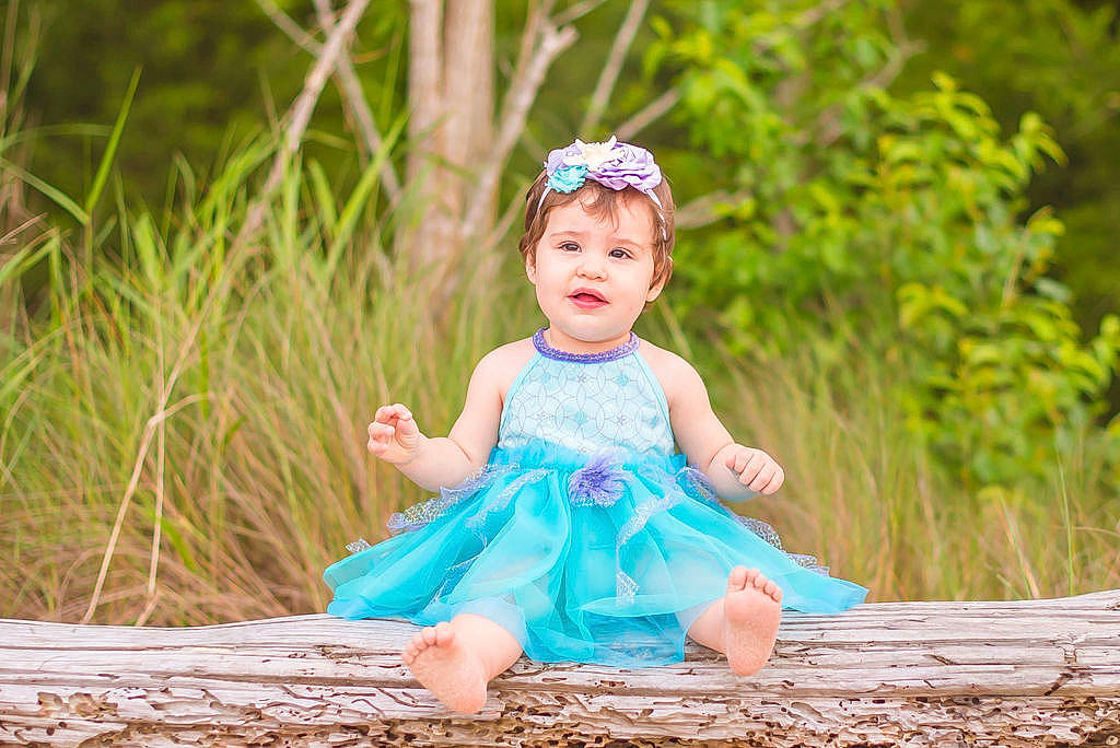Shelby is registered to the contest to win money with this photo: baby, baby_toddler_clothing, child, dress, eye, face, flash_photography, fun, grass, grass_family, happy, head, headgear, headpiece, headwear, leaf, people_in_nature, person, plant, purple